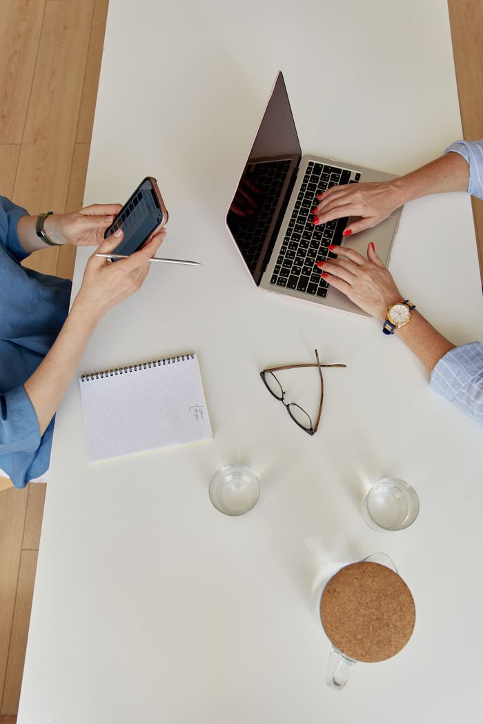 Two businesswomen collaborating in an office with laptop and smartphone.